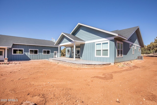 rear view of property with cooling unit, board and batten siding, a patio, and roof with shingles