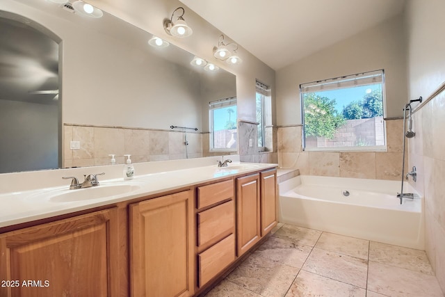 bathroom with tile patterned flooring, tile walls, a bathtub, vanity, and vaulted ceiling