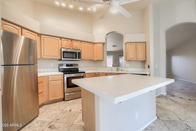 kitchen with a kitchen island, tile countertops, sink, stainless steel appliances, and light brown cabinets