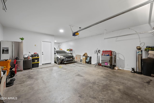 garage with a garage door opener and stainless steel refrigerator with ice dispenser