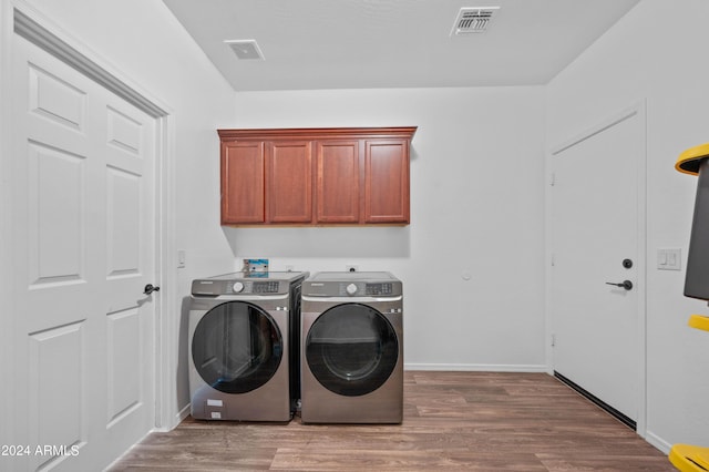 clothes washing area featuring washing machine and clothes dryer, hardwood / wood-style floors, and cabinets