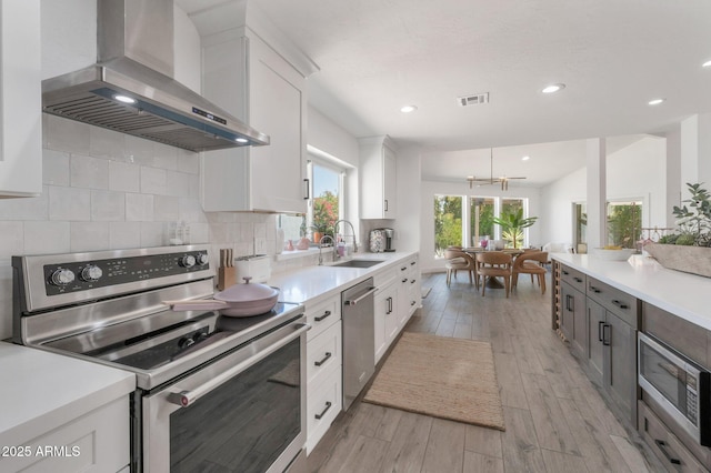 8719 E San Marino Dr, Scottsdale, AZ 85258 - kitchen featuring light wood finished floors, stainless steel appliances, backsplash, a sink, and wall chimney exhaust hood