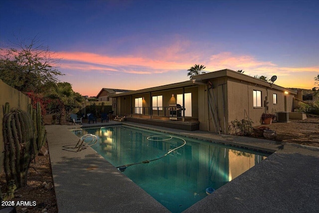 pool at dusk with a patio, cooling unit, a fenced backyard, and an outdoor pool