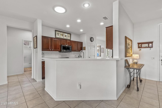 kitchen with light tile patterned flooring, kitchen peninsula, and tasteful backsplash