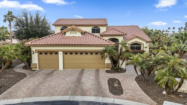mediterranean / spanish-style house featuring stucco siding, an attached garage, a tile roof, and decorative driveway