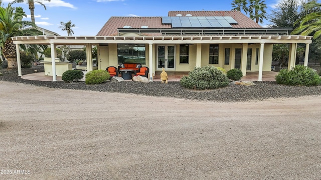 rear view of property featuring a patio area, stucco siding, french doors, and solar panels