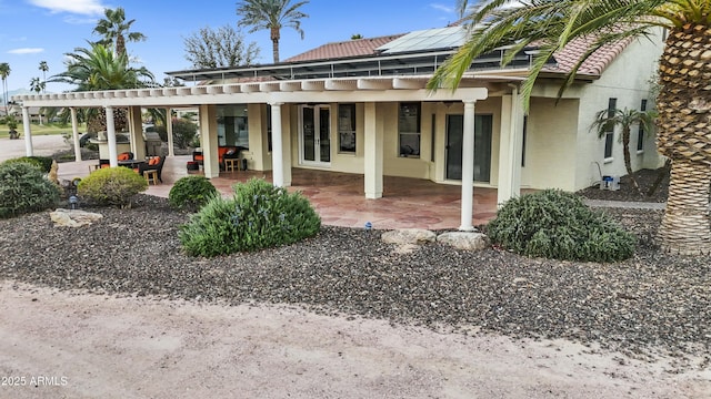 rear view of property featuring stucco siding, a patio, roof mounted solar panels, and a pergola