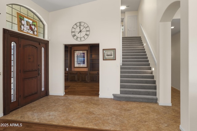 entryway featuring tile patterned flooring, stairway, baseboards, and arched walkways