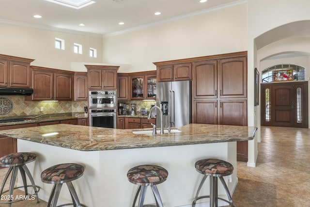 kitchen featuring under cabinet range hood, appliances with stainless steel finishes, a breakfast bar area, and a sink