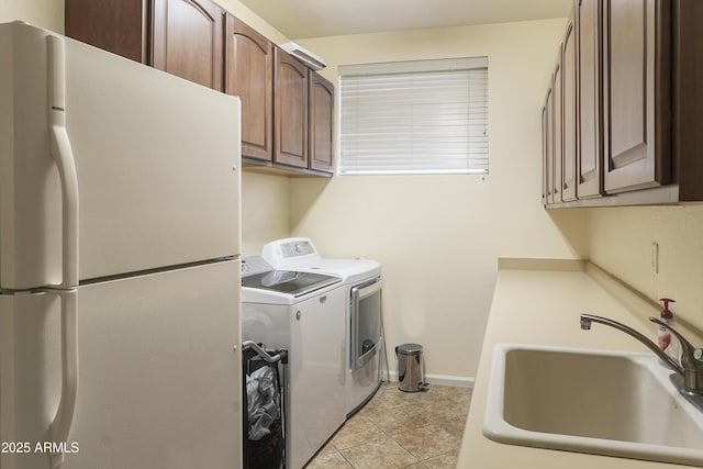 laundry area featuring a sink, cabinet space, light tile patterned floors, baseboards, and washing machine and clothes dryer