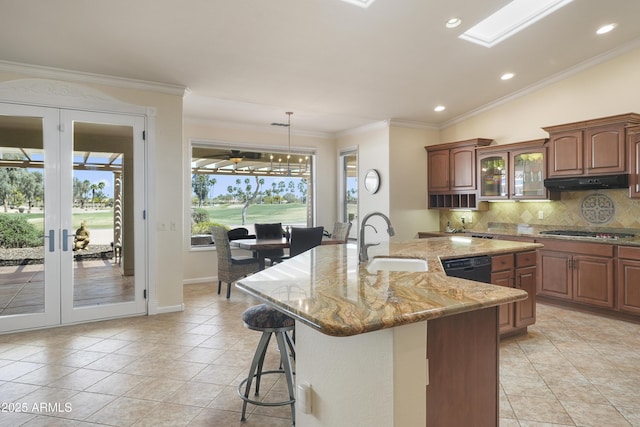 kitchen with stainless steel gas cooktop, a sink, under cabinet range hood, a kitchen breakfast bar, and tasteful backsplash