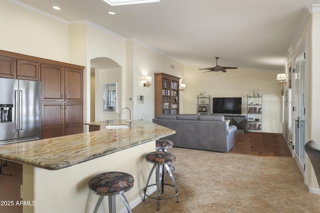 kitchen featuring a sink, light stone counters, arched walkways, a breakfast bar area, and ceiling fan