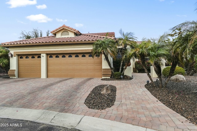 mediterranean / spanish-style house with a garage, decorative driveway, stucco siding, and a tiled roof
