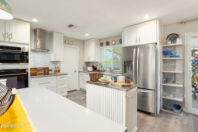 kitchen with white cabinetry, stainless steel appliances, wall chimney range hood, and light hardwood / wood-style floors