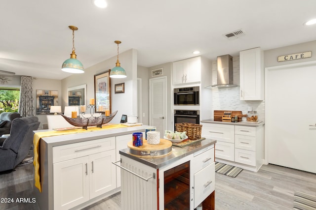 kitchen featuring double wall oven, wall chimney range hood, a kitchen island, and visible vents