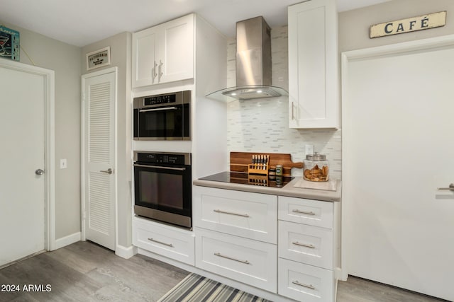 kitchen featuring tasteful backsplash, light wood-style floors, black electric stovetop, wall chimney range hood, and white cabinetry