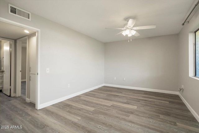 empty room featuring a ceiling fan, wood finished floors, visible vents, and baseboards