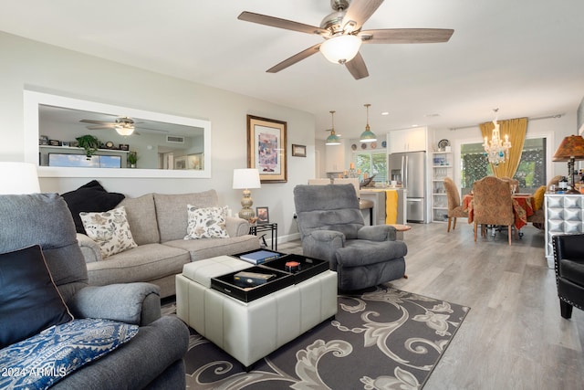 living area featuring ceiling fan with notable chandelier, light wood finished floors, and visible vents