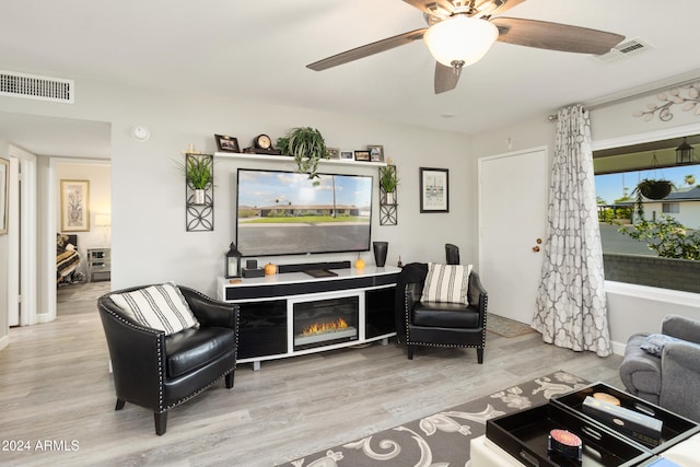 living area featuring a ceiling fan, visible vents, wood finished floors, and a glass covered fireplace