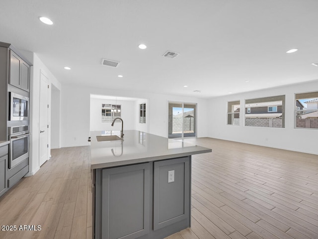 17815 W Denton Ave, Litchfield Park, AZ 85340 - kitchen with appliances with stainless steel finishes, a sink, gray cabinetry, light wood finished floors, and an island with sink