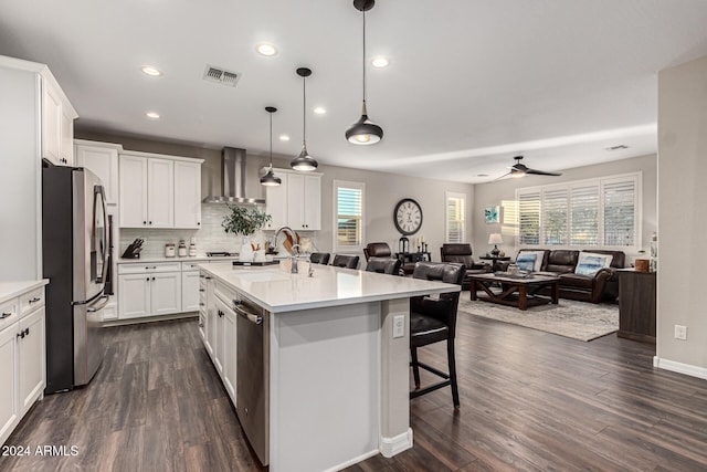 kitchen featuring white cabinetry, appliances with stainless steel finishes, wall chimney exhaust hood, and a center island with sink