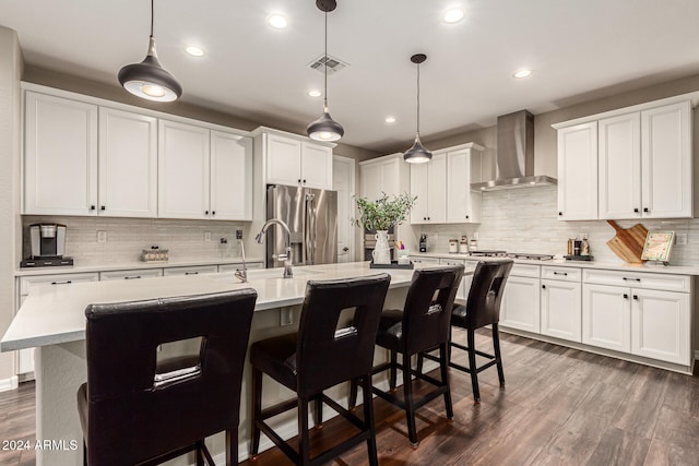 kitchen featuring stainless steel appliances, decorative light fixtures, an island with sink, dark wood-type flooring, and wall chimney exhaust hood