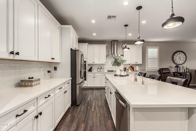 kitchen featuring a center island with sink, white cabinets, wall chimney exhaust hood, sink, and appliances with stainless steel finishes