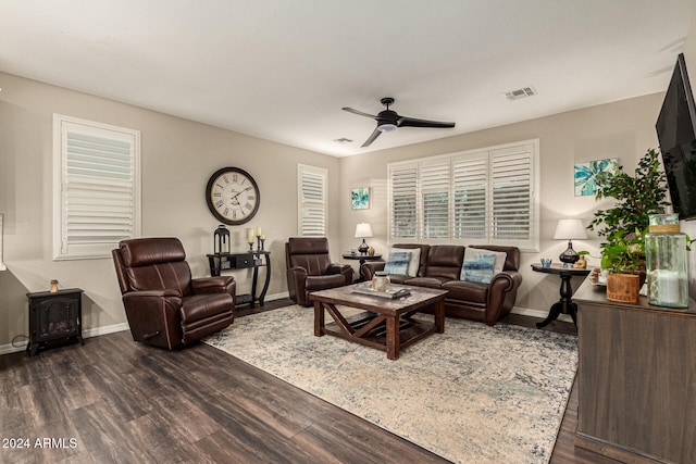 living room featuring dark wood-type flooring, ceiling fan, a healthy amount of sunlight, and a wood stove