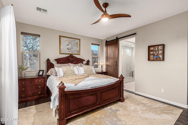 bedroom with ensuite bathroom, light hardwood / wood-style flooring, a barn door, and ceiling fan