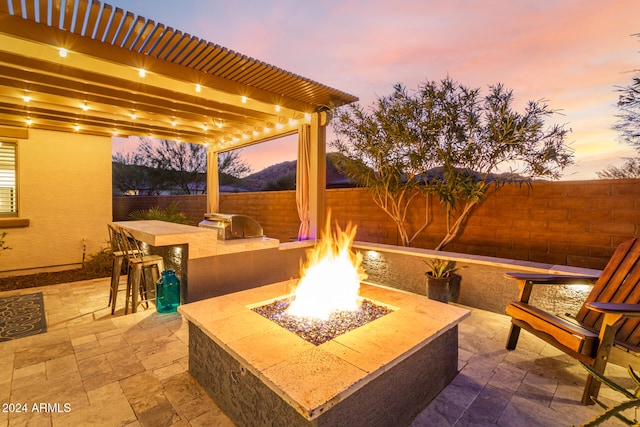 patio terrace at dusk with area for grilling, exterior bar, and an outdoor fire pit