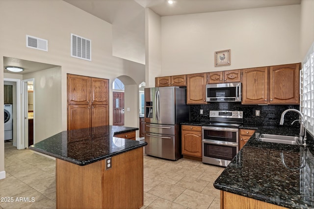 kitchen with sink, dark stone counters, a center island, high vaulted ceiling, and stainless steel appliances