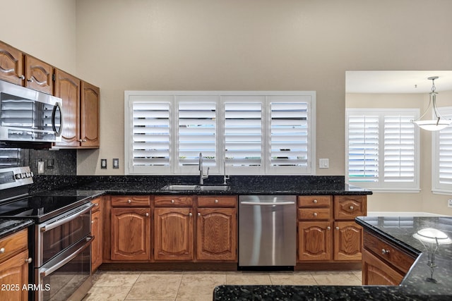 kitchen featuring light tile patterned floors, sink, dark stone countertops, pendant lighting, and stainless steel appliances