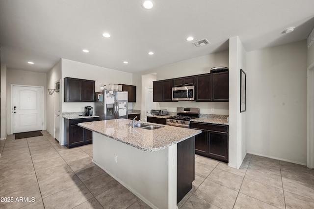 30963 W Columbus Ave, Buckeye, AZ 85396 - kitchen featuring appliances with stainless steel finishes, a sink, a kitchen island with sink, dark brown cabinetry, and light tile patterned floors