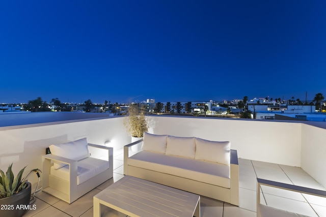 patio at night with a view of city lights, a balcony, and outdoor lounge area