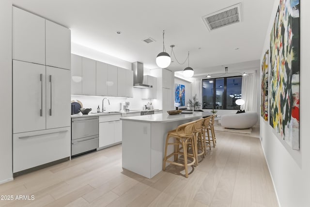 kitchen featuring a center island, dishwasher, visible vents, and wall chimney range hood