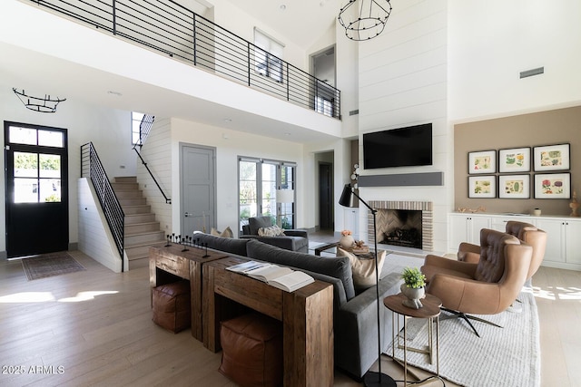 living room featuring a high ceiling, a brick fireplace, a notable chandelier, and light hardwood / wood-style flooring