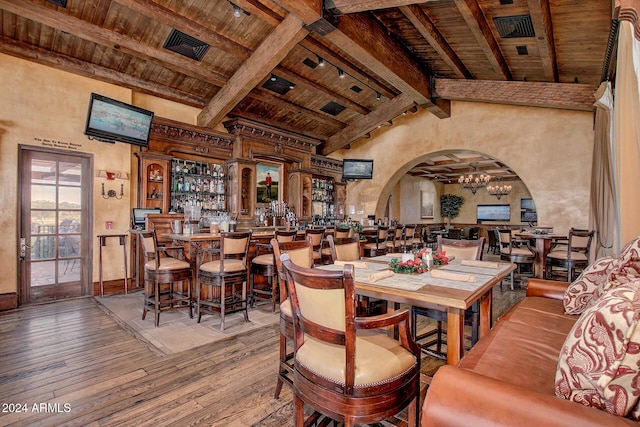 dining area with rail lighting, lofted ceiling with beams, hardwood / wood-style flooring, wooden ceiling, and bar