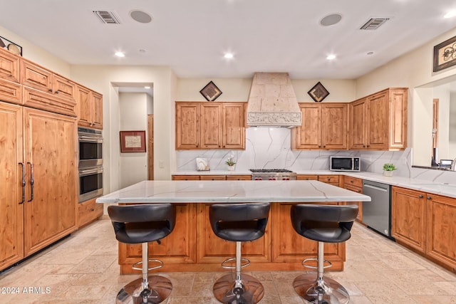 kitchen with appliances with stainless steel finishes, tasteful backsplash, a kitchen island, custom range hood, and a breakfast bar area