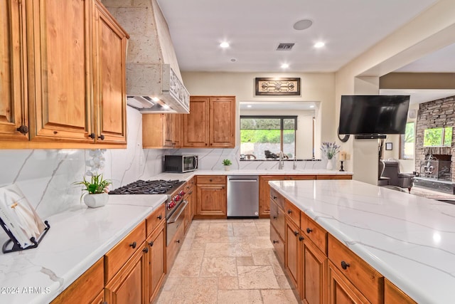 kitchen with tasteful backsplash, stainless steel dishwasher, wall chimney exhaust hood, and light stone counters