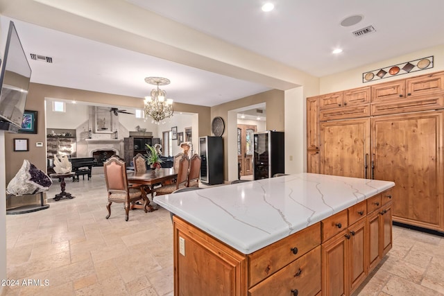 kitchen with black fridge, light stone counters, ceiling fan with notable chandelier, paneled built in fridge, and a kitchen island