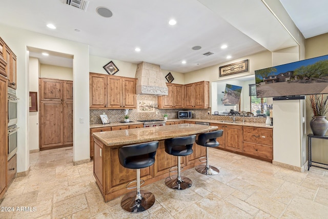 kitchen with light stone countertops, tasteful backsplash, custom range hood, a center island, and a breakfast bar area