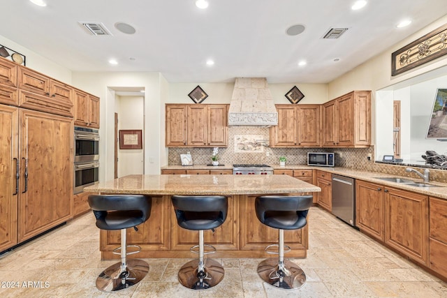 kitchen featuring sink, a kitchen breakfast bar, premium range hood, a kitchen island, and appliances with stainless steel finishes