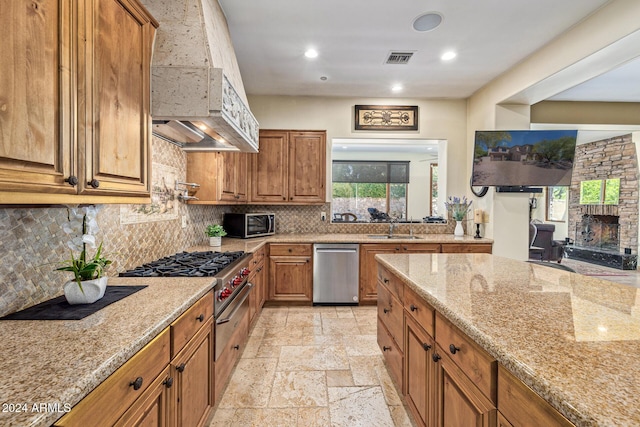 kitchen with a stone fireplace, sink, stainless steel dishwasher, a wealth of natural light, and light stone counters