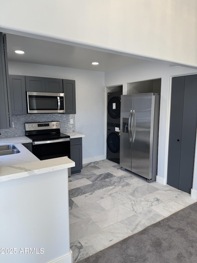 kitchen featuring sink, stacked washer / dryer, stainless steel appliances, and tasteful backsplash