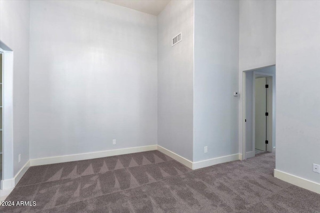 spare room featuring a towering ceiling and dark carpet