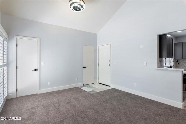 unfurnished living room with high vaulted ceiling, sink, and light carpet