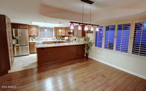 kitchen with kitchen peninsula, pendant lighting, decorative backsplash, appliances with stainless steel finishes, and light wood-type flooring