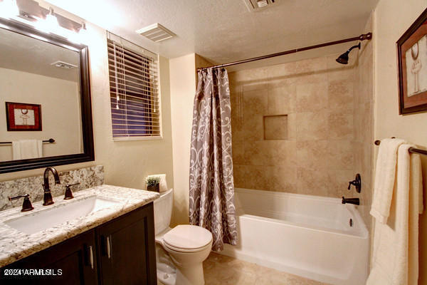 full bathroom with toilet, a textured ceiling, vanity, and shower / tub combo with curtain