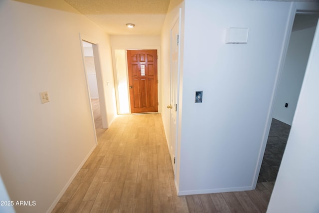 hallway with light hardwood / wood-style floors and a textured ceiling