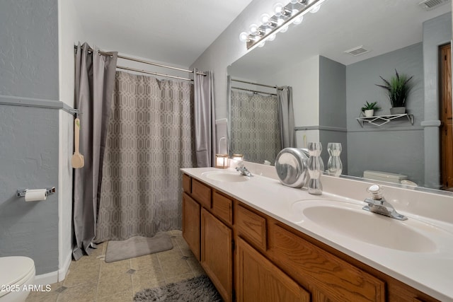 bathroom with toilet, double vanity, and a sink